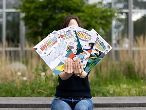 Person holding up the four English-language CASA science comics